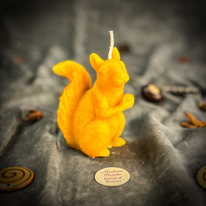 Yellow squirrel-shaped candle on a textured surface with a brand label.