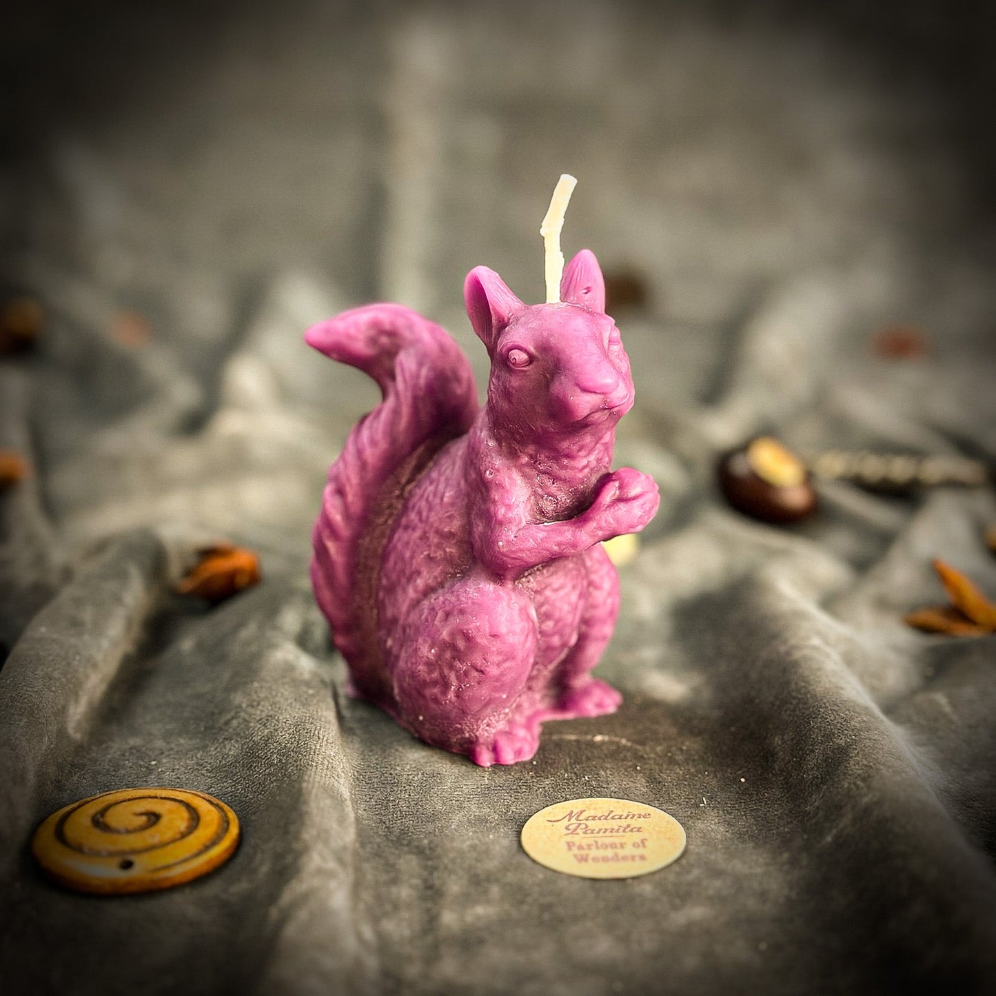 Pink squirrel-shaped candle on a stone surface with blurred background