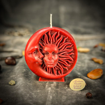 Red candle with sun and moon design on a dark surface, featuring a brand label.