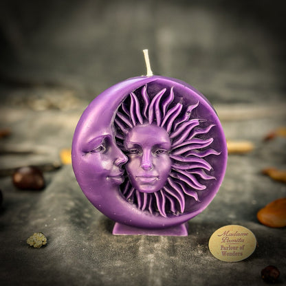 Purple candle with sun and moon design on a dark surface