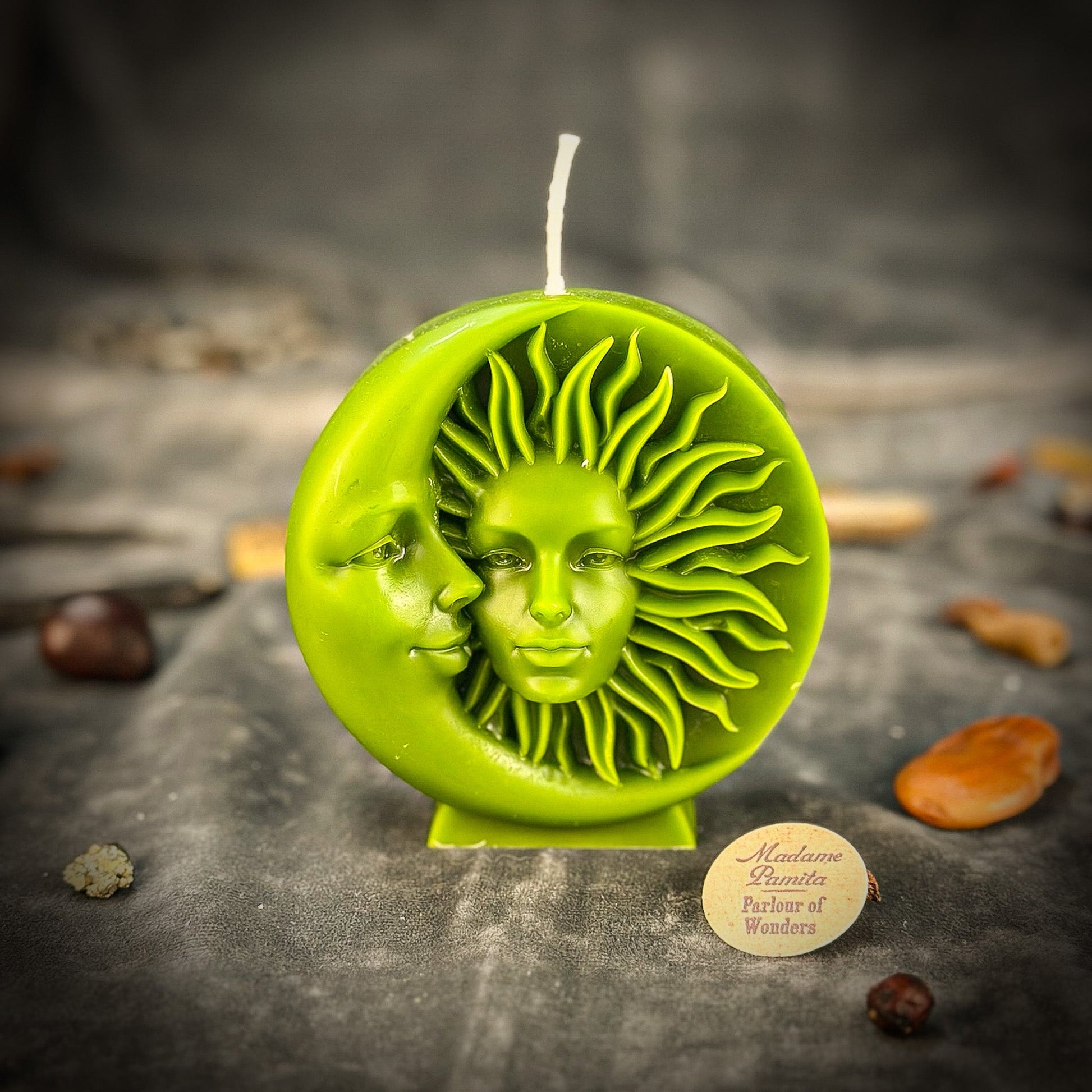 Green sun and moon candle on a dark surface with a brand label.