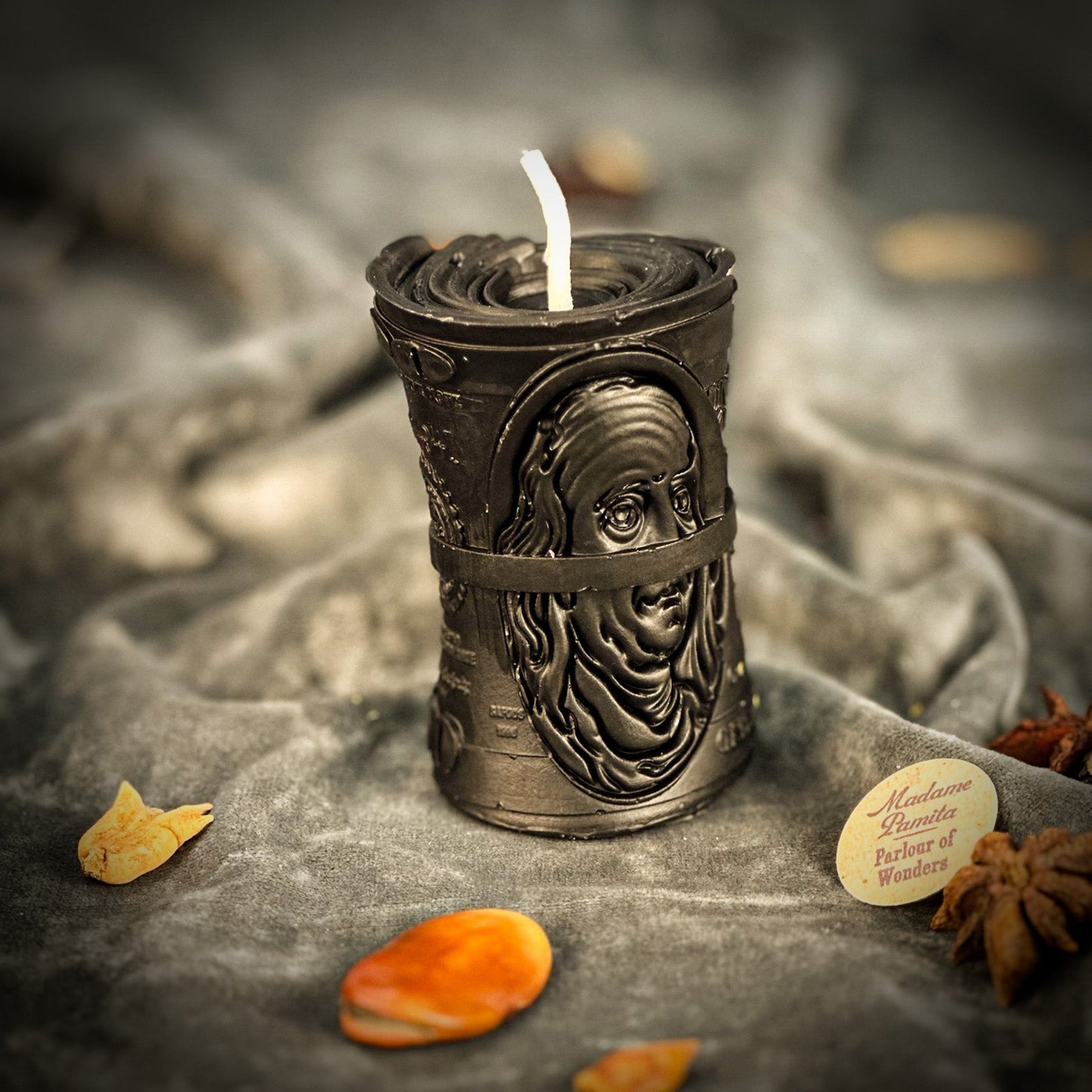 Decorative candle holder with a face design on a textured surface with dried leaves and star anise.
