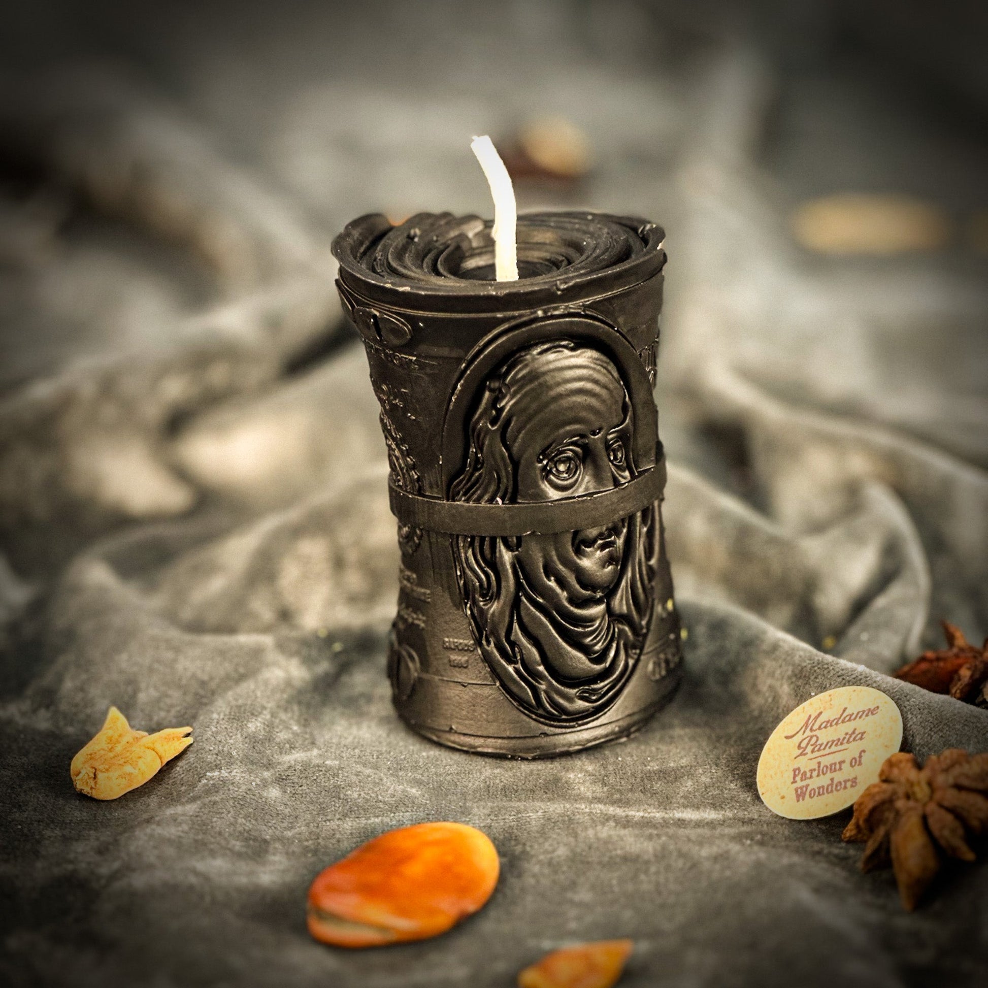 Decorative candle holder with a face design on a textured surface with dried leaves and star anise.