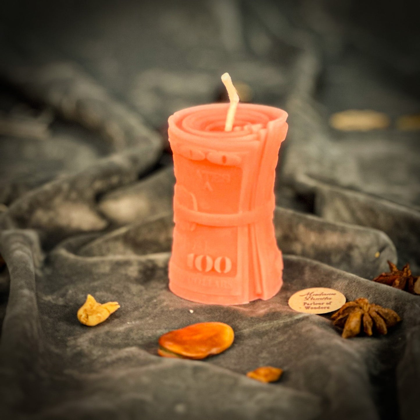 Pink candle shaped like a bottle with a flame on a dark fabric background