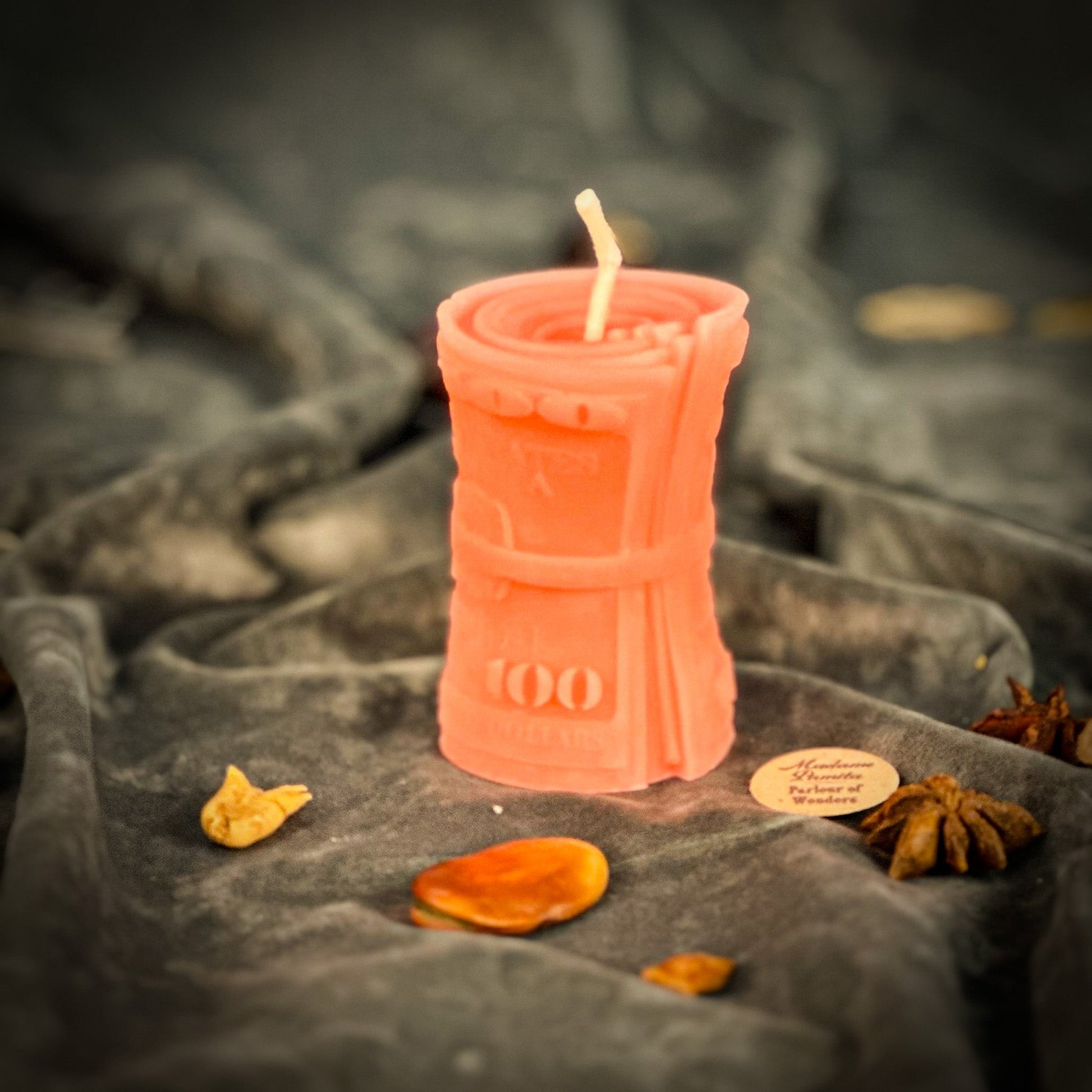 Pink candle shaped like a bottle with a flame on a dark fabric background