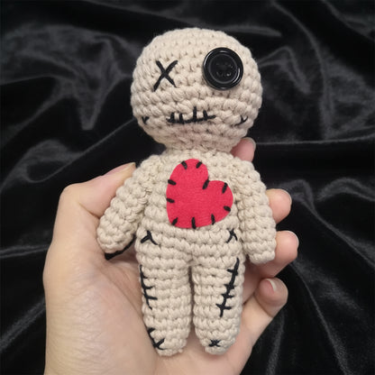 Hand holding a small crochet doll with a red heart on a plain background