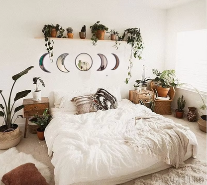Cozy bedroom with white bedding, plants, and decorative moon phases on the wall.