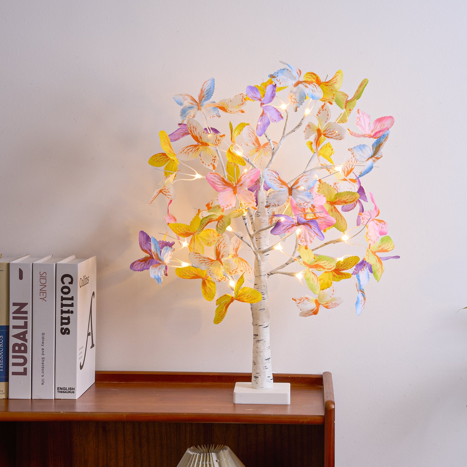 Decorative LED tree with colorful leaves on a wooden shelf against a white wall.