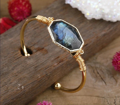 Gold bracelet with a blue gemstone on a wooden surface with flowers.