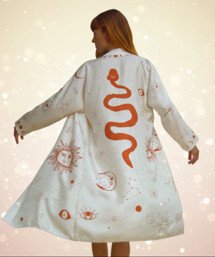 Person wearing a white dress with red snake and sun designs in a room.