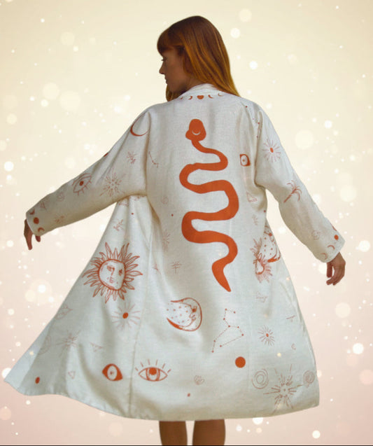 Person wearing a white dress with red snake and sun designs in a room.