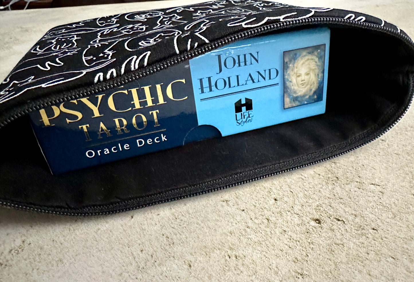 Zipped pouch containing a Psychic Tarot Oracle Deck and a book by John Holland on a light surface.