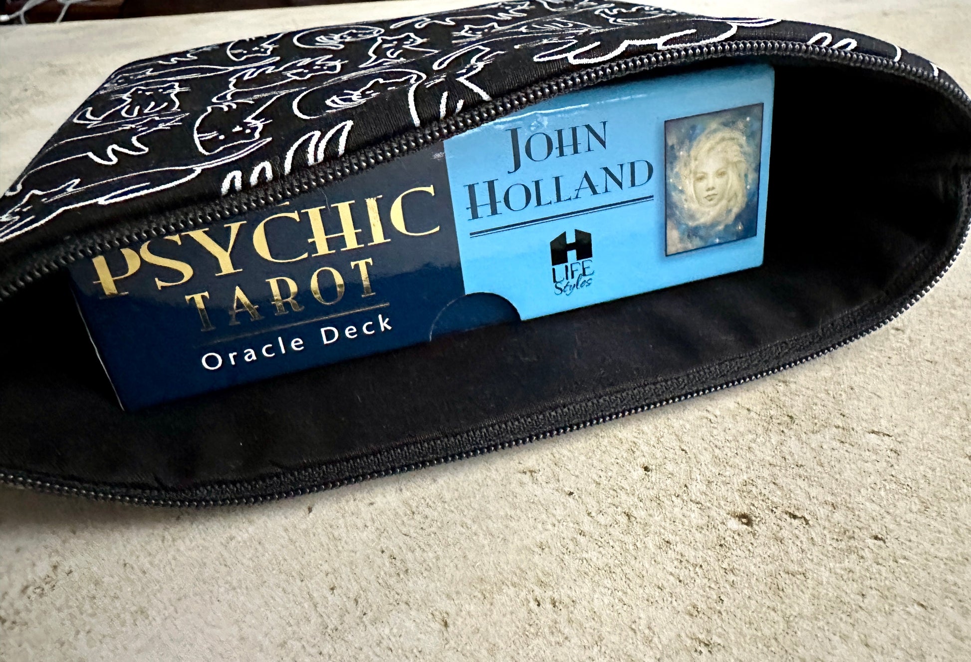 Zipped pouch containing a Psychic Tarot Oracle Deck and a book by John Holland on a light surface.