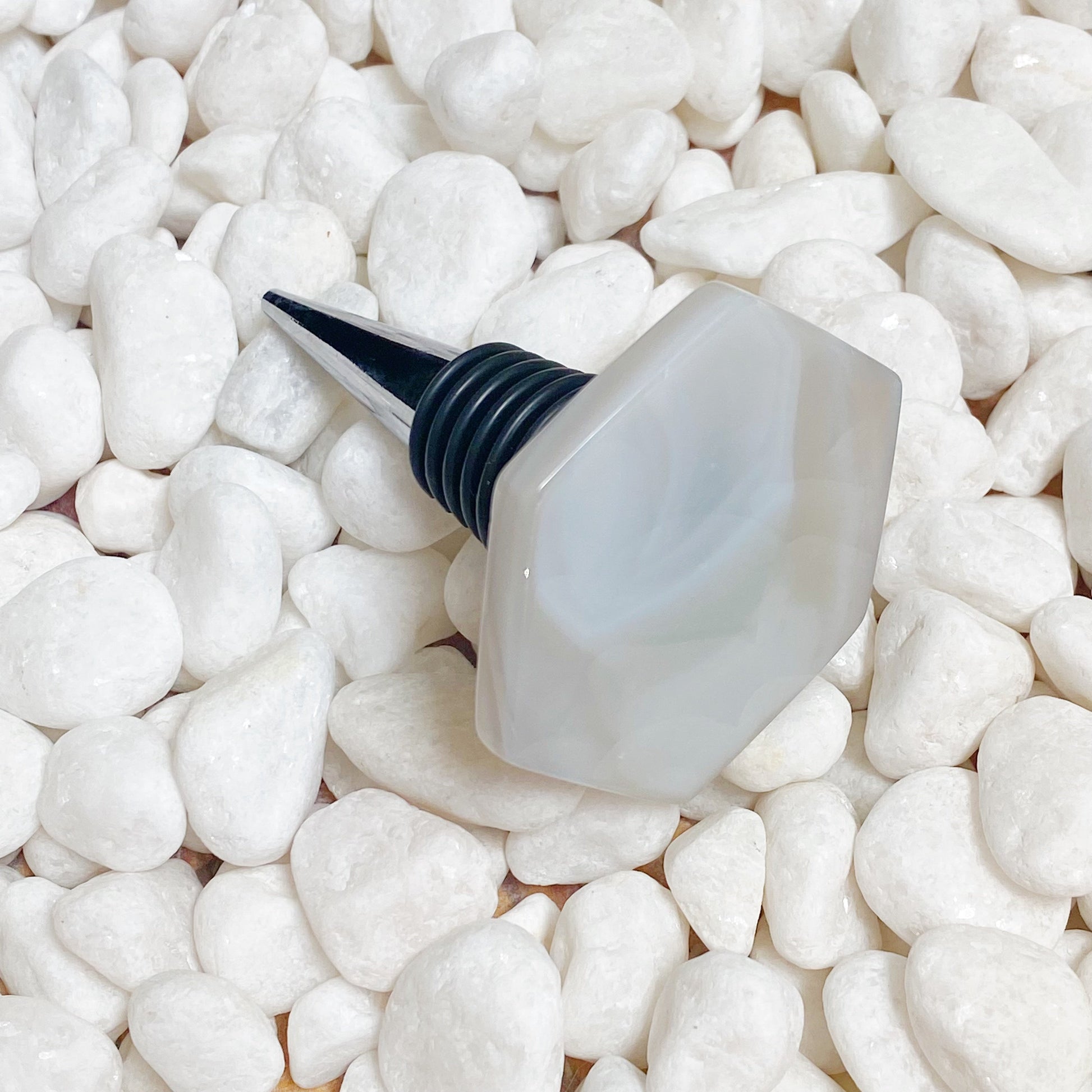 White bottle stopper with black nozzle on a bed of small white stones