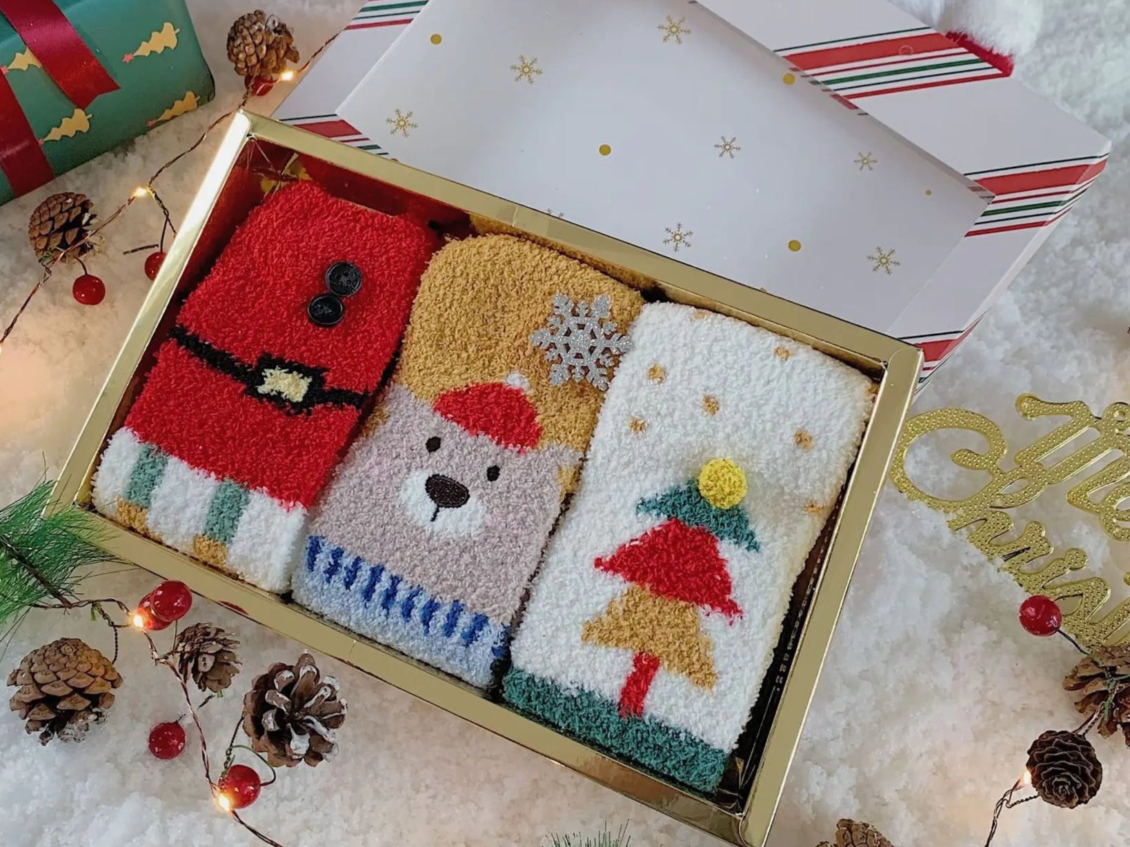 Set of three Christmas-themed socks in a decorative box with festive decorations around.