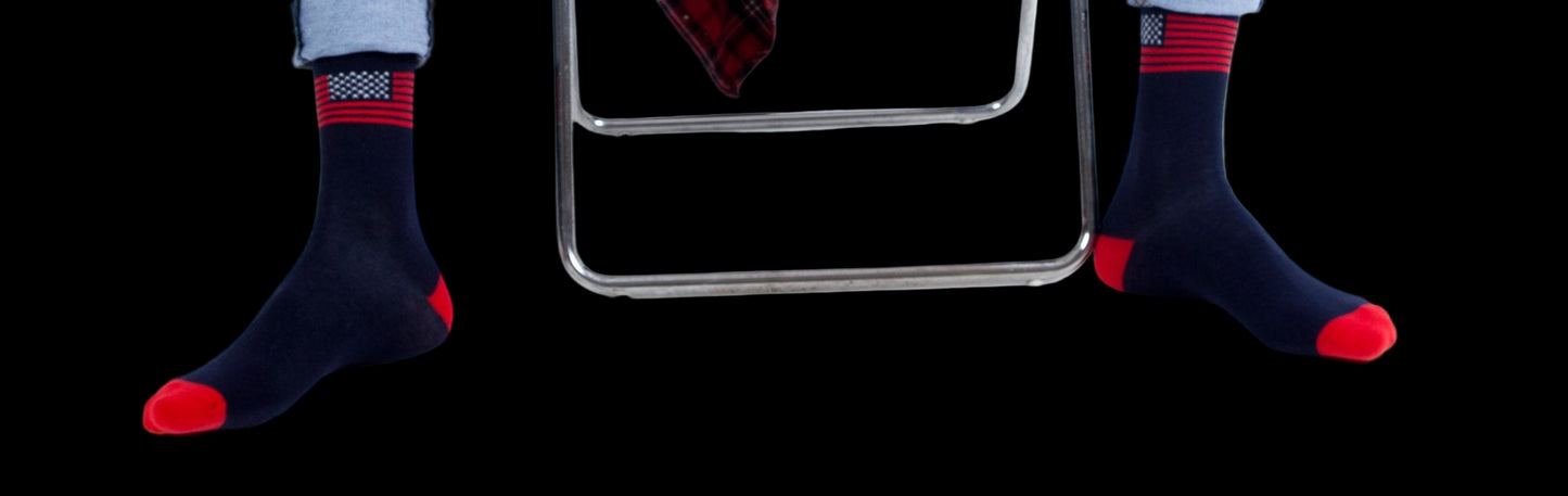 Person wearing blue jeans, a red plaid shirt, and dark socks with red accents sitting on a white chair.