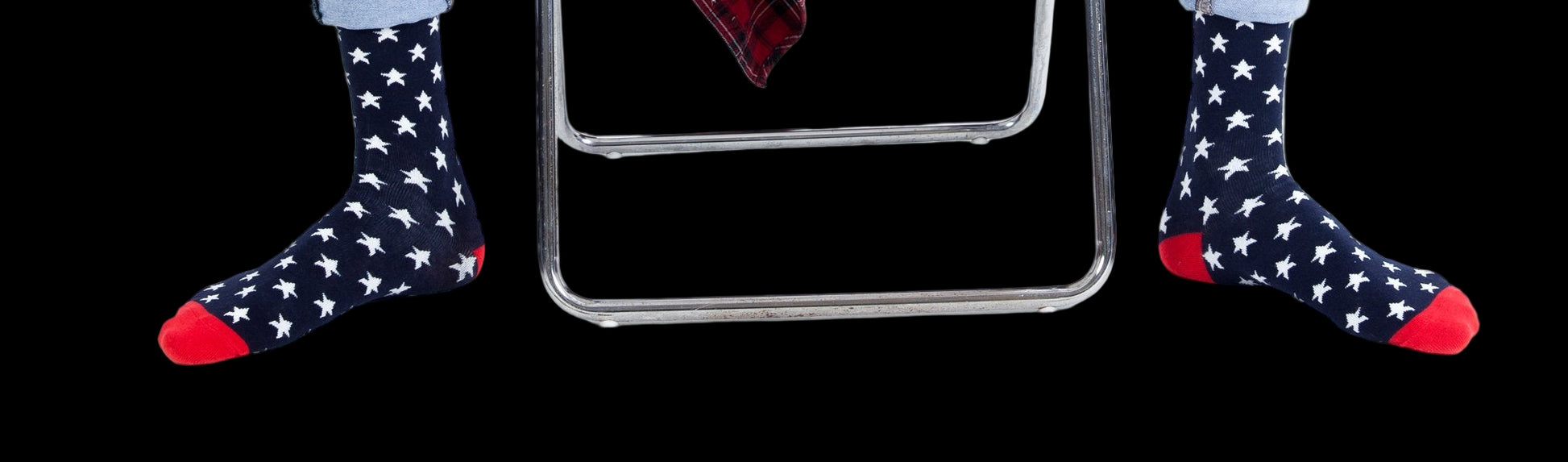 Person sitting on a chair wearing blue jeans, a plaid shirt, and star-patterned socks with red accents.