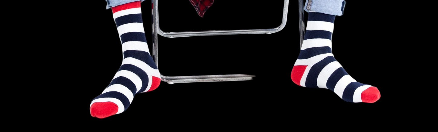 Person wearing blue jeans and striped socks sitting on a white chair with a red plaid shirt draped over their legs.