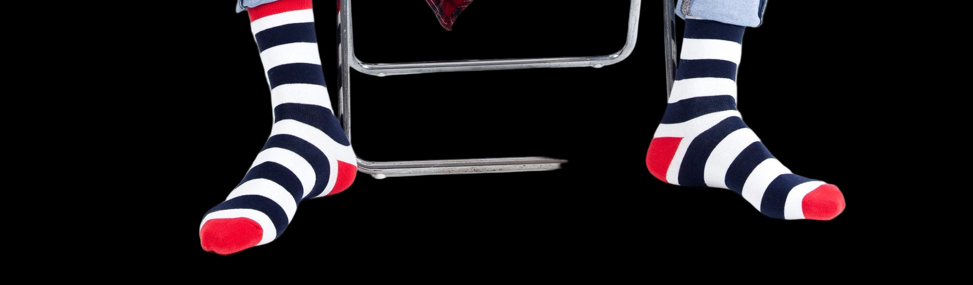 Person wearing blue jeans and striped socks sitting on a white chair with a red plaid shirt draped over their legs.