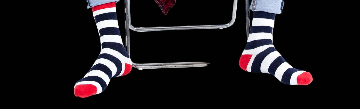 Person wearing blue jeans and striped socks sitting on a white chair with a red plaid shirt draped over their legs.