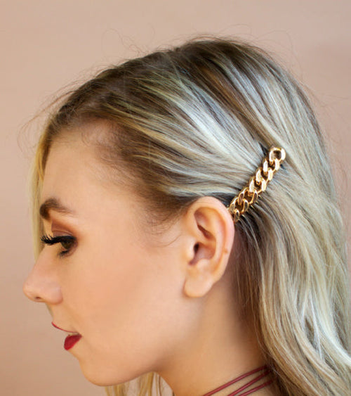 Woman with blonde hair featuring a gold chain accessory against a beige background