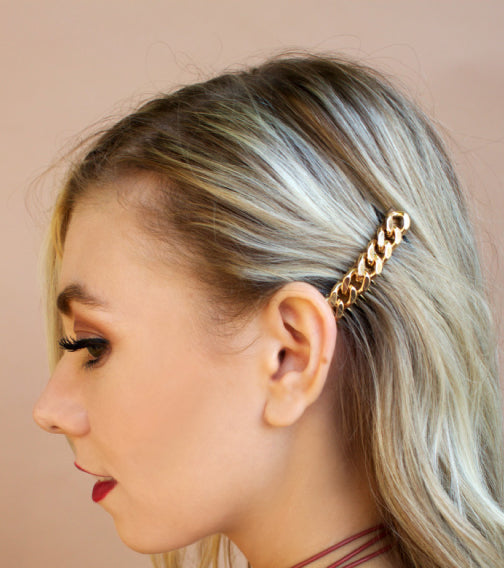 Woman with blonde hair featuring a gold chain accessory against a beige background