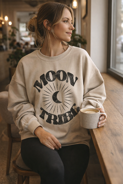 Woman wearing a 'Moon Tribe' sweatshirt holding a coffee mug in a casual setting.