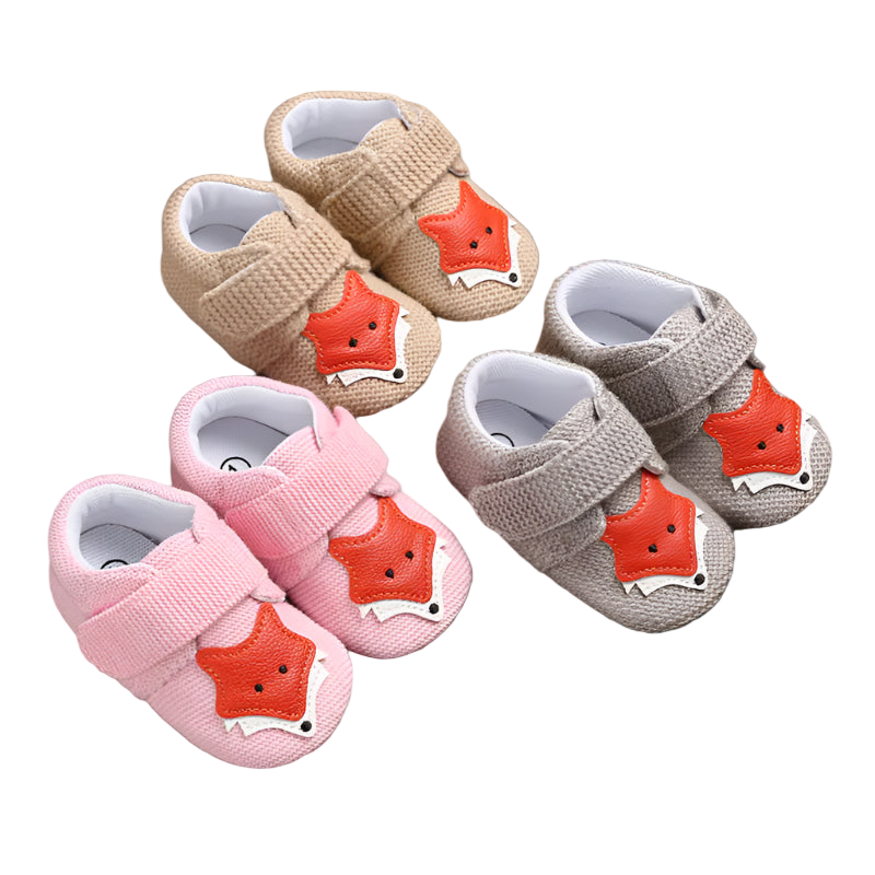 Set of baby shoes with fox face design on a wooden surface