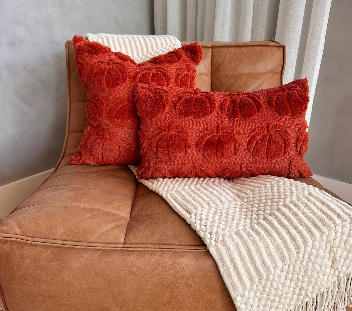 Brown leather chair with red textured pillows and a white blanket
