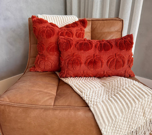 Brown leather chair with red textured pillows and a white blanket
