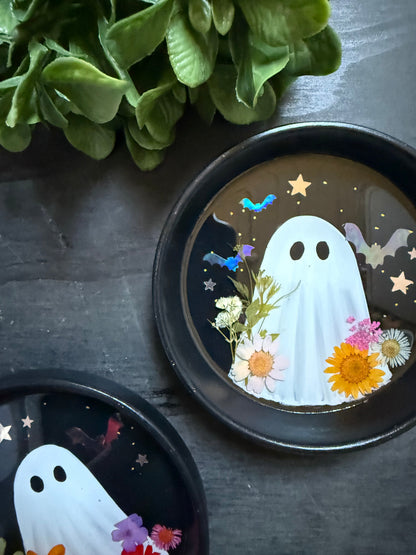 Decorative plate with a ghost design surrounded by flowers on a dark surface.