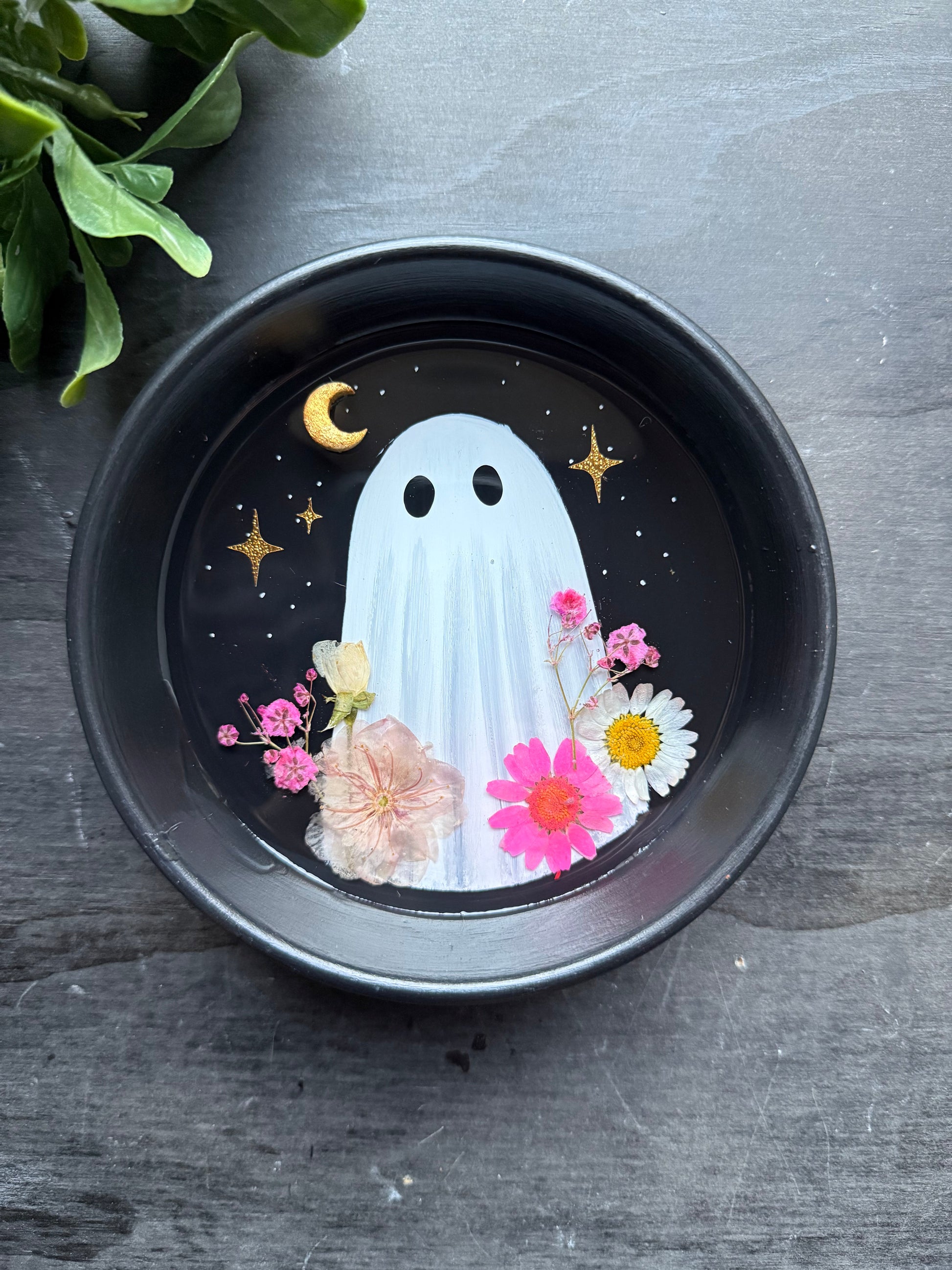 Decorative plate with a ghost and flowers design on a dark surface