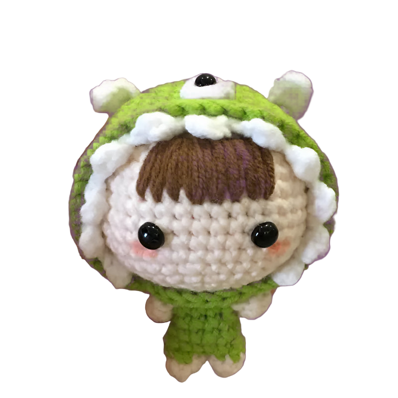Hand holding a small crochet toy with green outfit and white accents on a textured surface