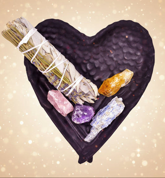 Black heart-shaped dish with smudge sticks, crystals, and stones on a white background