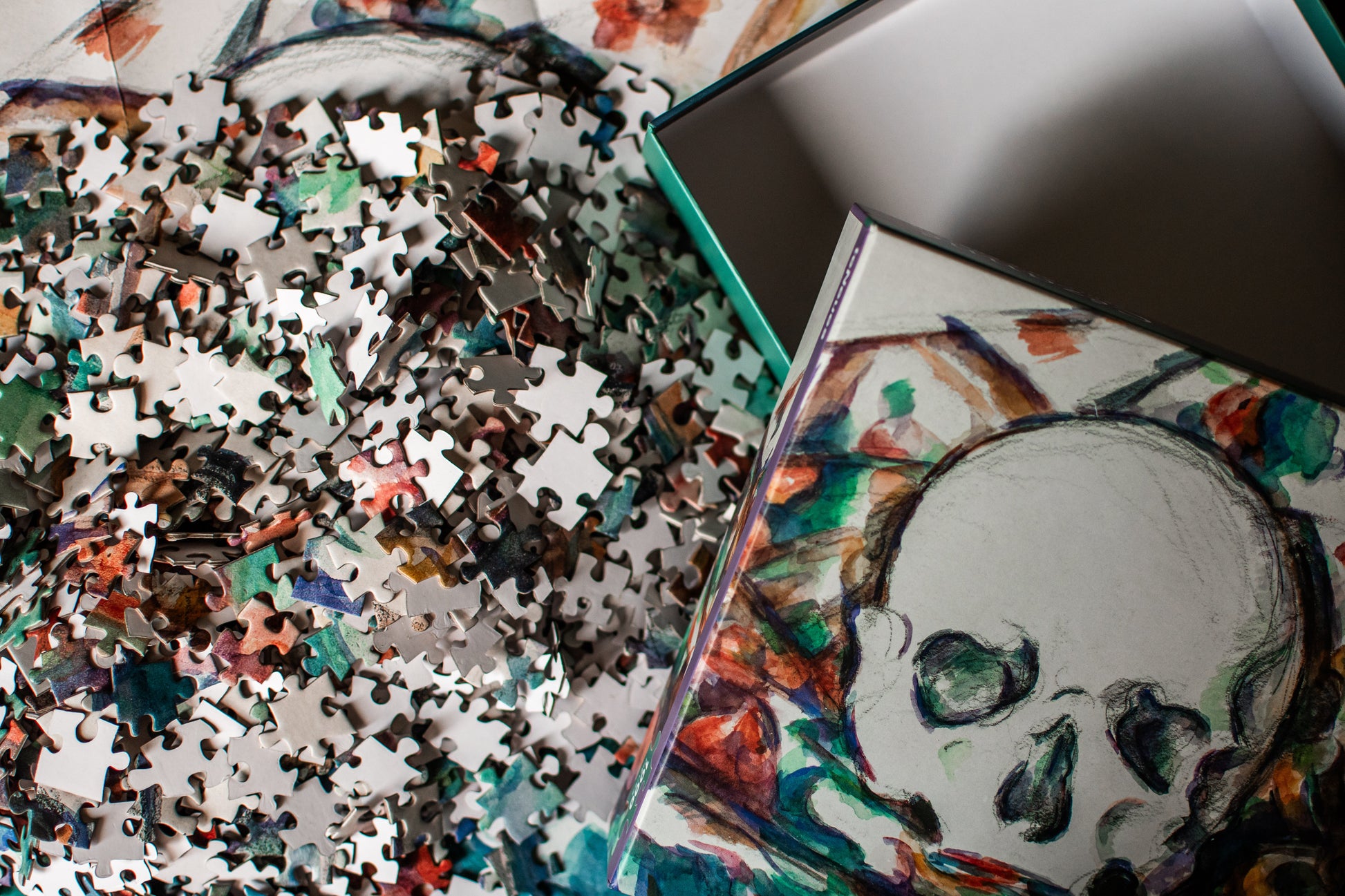 A close-up of a jigsaw puzzle box and scattered puzzle pieces featuring a colorful skull illustration on a white background.