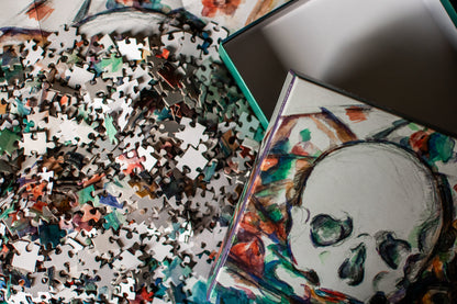 A close-up of a jigsaw puzzle box and scattered puzzle pieces featuring a colorful skull illustration on a white background.