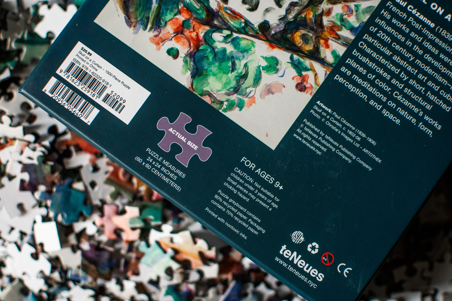 The back of a jigsaw puzzle box shown at an angle, surrounded by loose puzzle pieces. The box is dark teal with a large multicolor abstract artwork panel, a puzzle piece icon, a barcode, and the teNeues brand logo near the bottom.