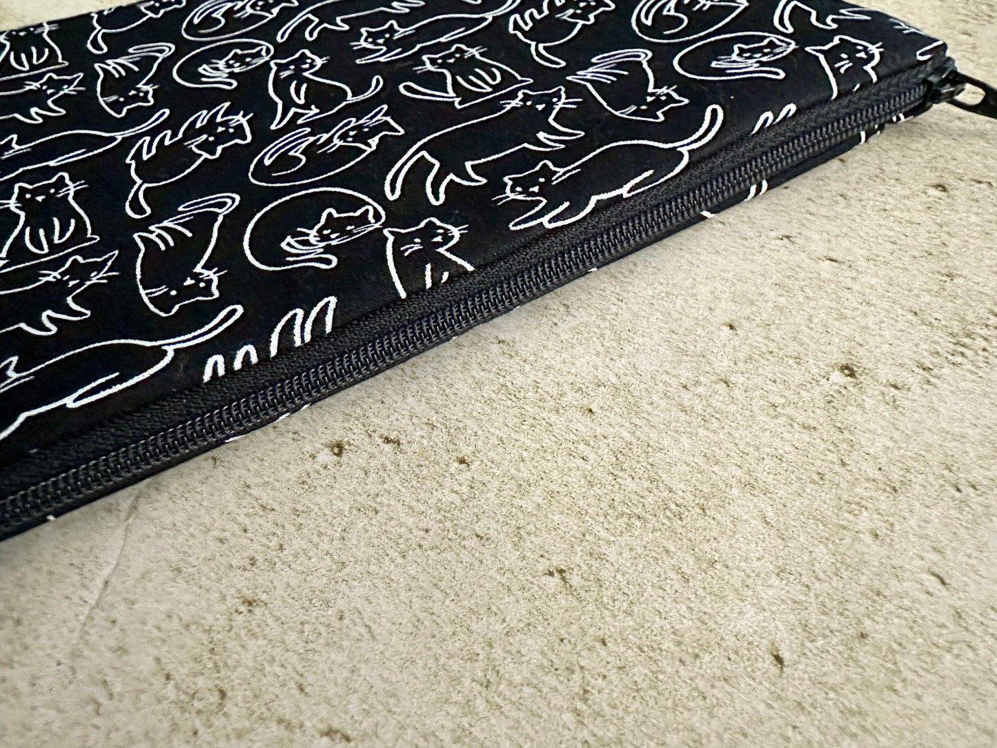 Black pouch with white cat illustrations on a beige surface