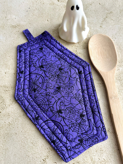 Purple oven mitt with Halloween design, wooden spoon, and ghost on a beige surface