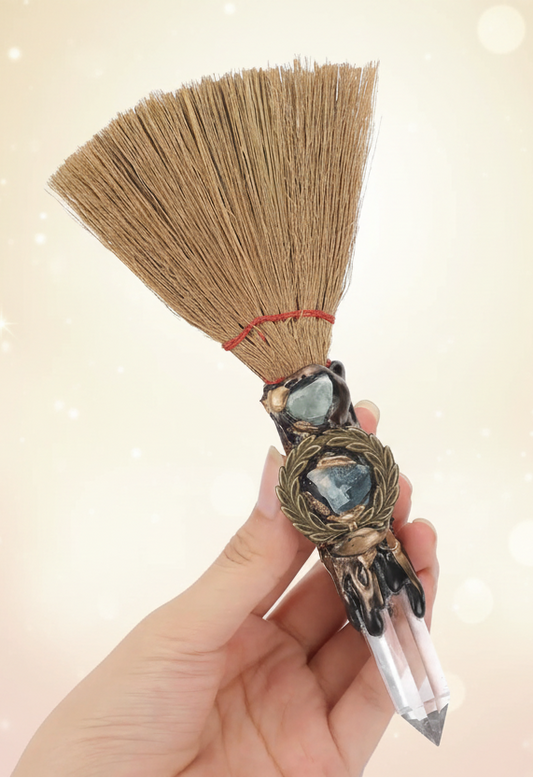 Hand holding a broom with a decorative handle against a white background