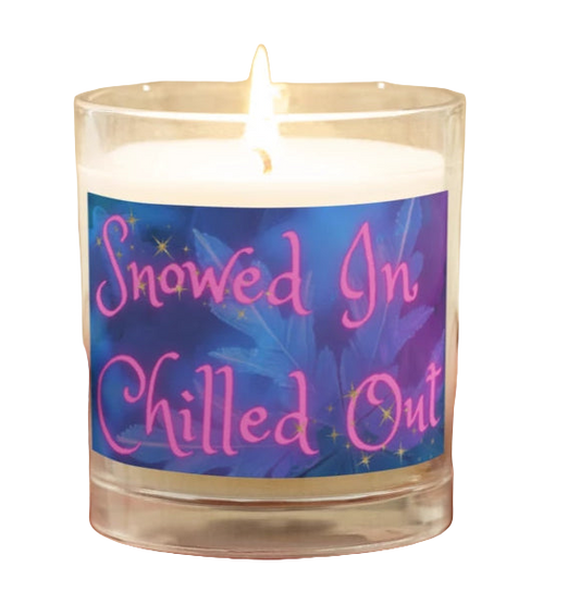 Candle with a label reading 'Snowed In Chilled Out' held by a person wearing a beige sweater.