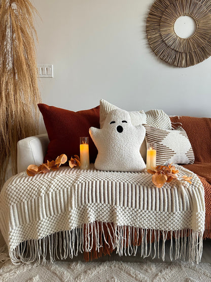 Decorative setup with a couch, pillows, candles, and a blanket in a cozy living room.