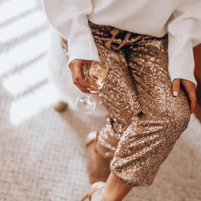 Person wearing a gold sequin skirt and holding a glass of champagne.