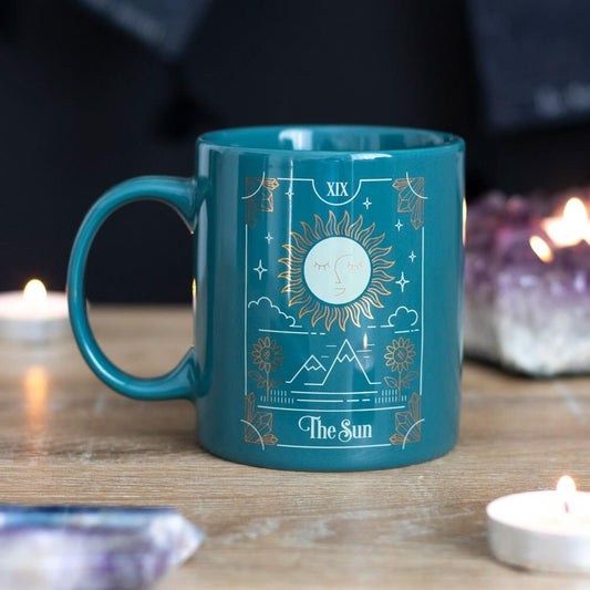 Teal mug with celestial design on a wooden surface with candles and crystals.