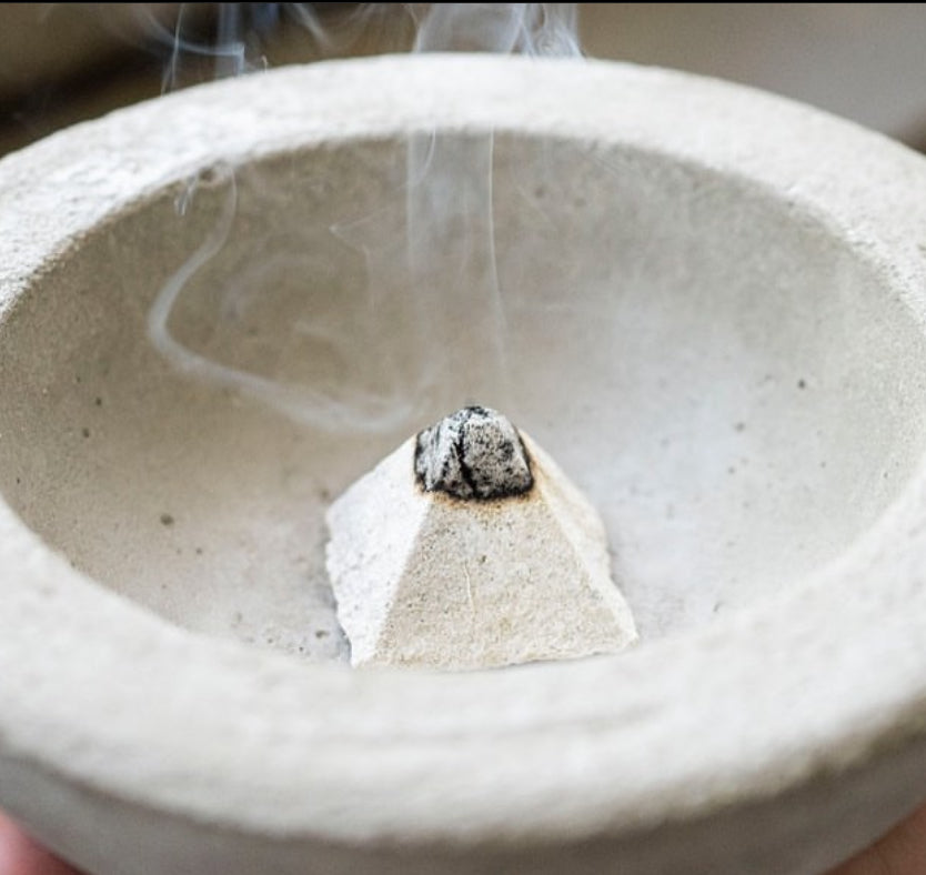 Incense stick burning in a ceramic bowl with smoke rising.
