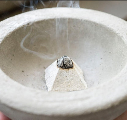 Incense stick burning in a ceramic bowl with smoke rising.
