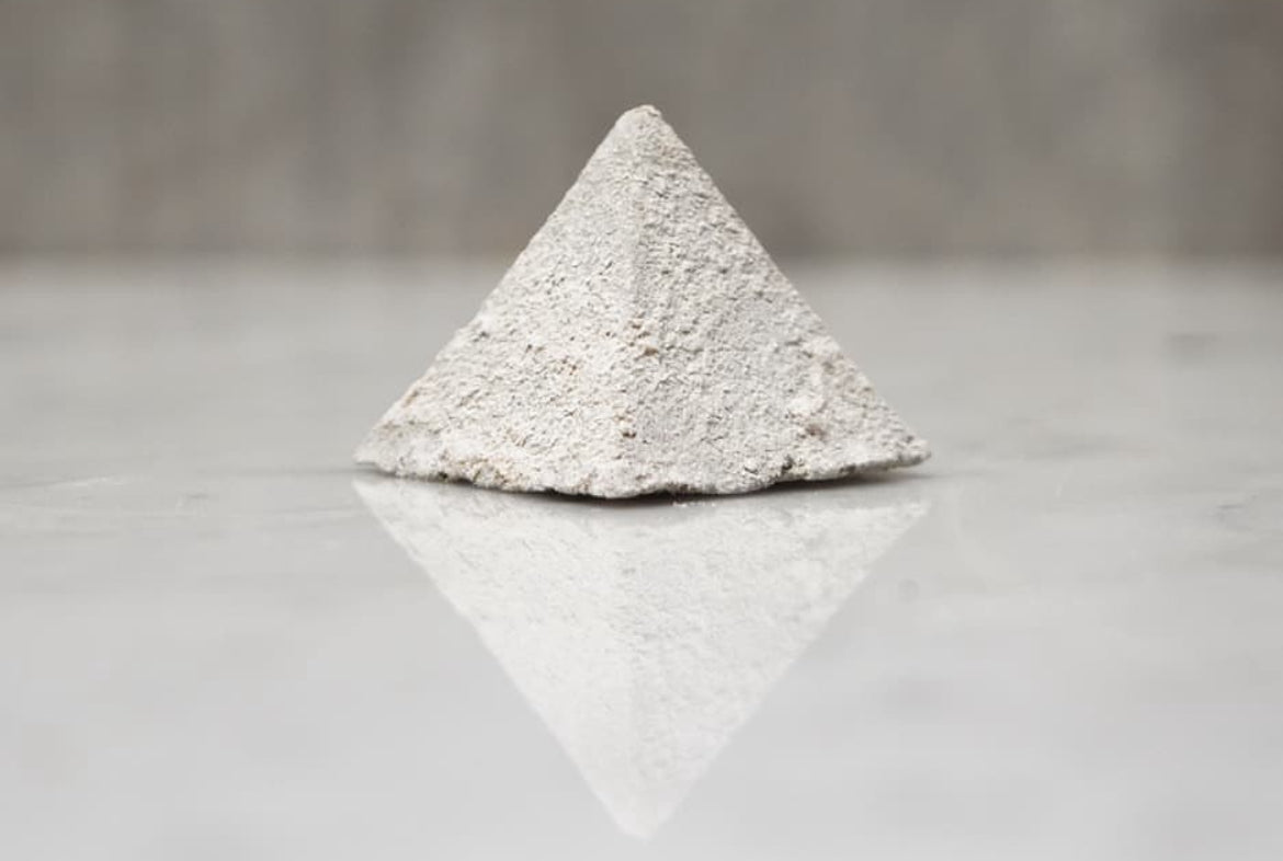 Pyramid-shaped object made of light gray material on a reflective surface with a neutral background