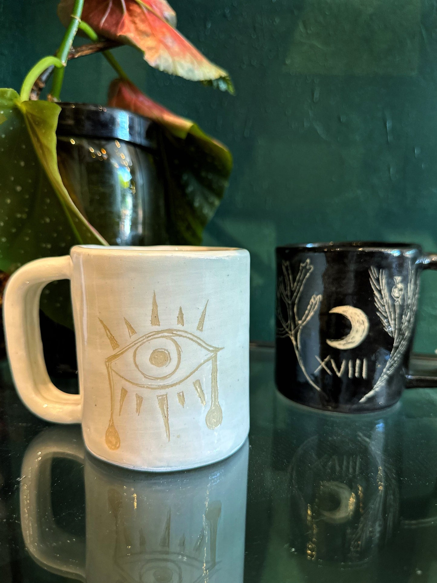 Two mugs with decorative designs on a reflective surface.