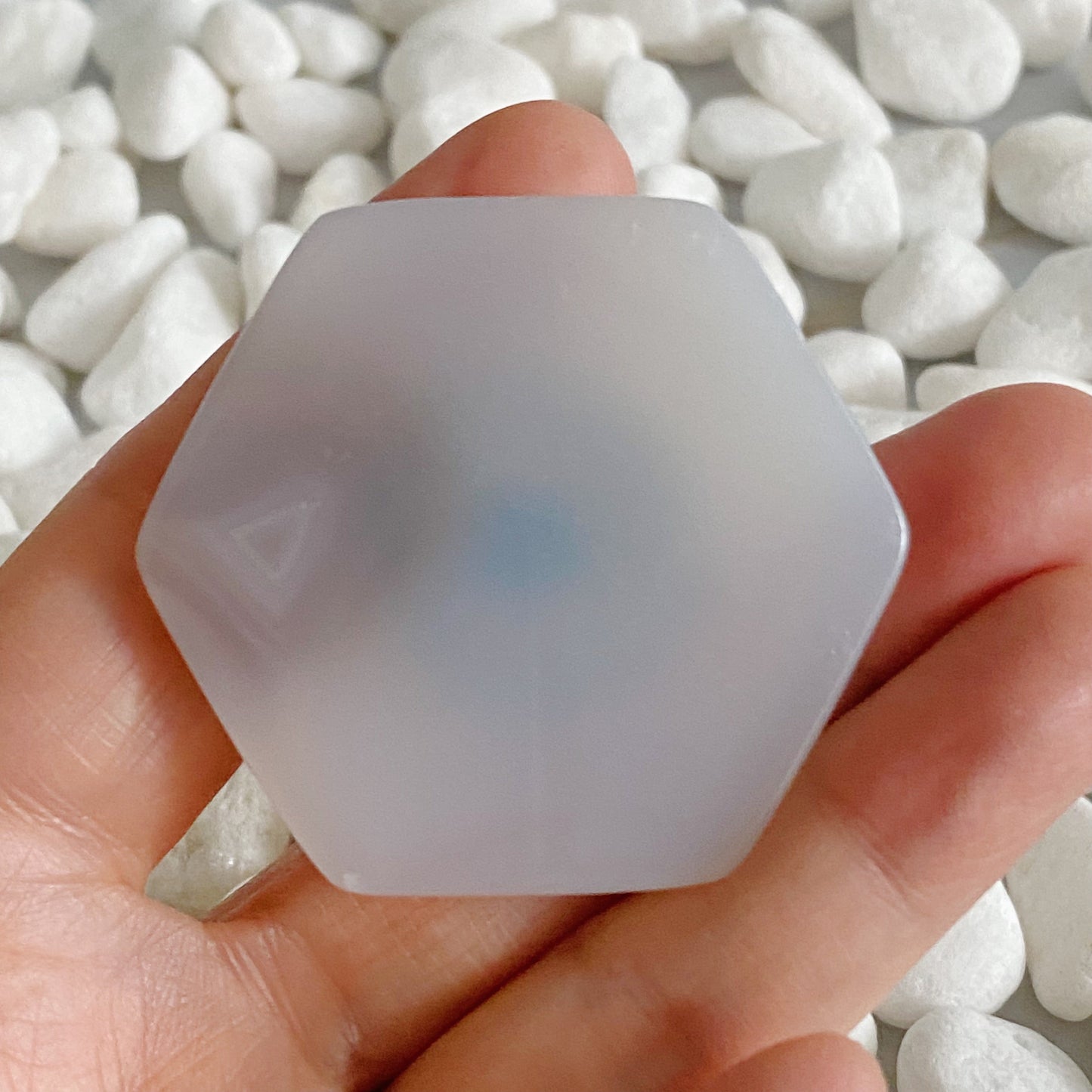 Clear silicone hexagonal object held in a hand with a blurred background of white stones.