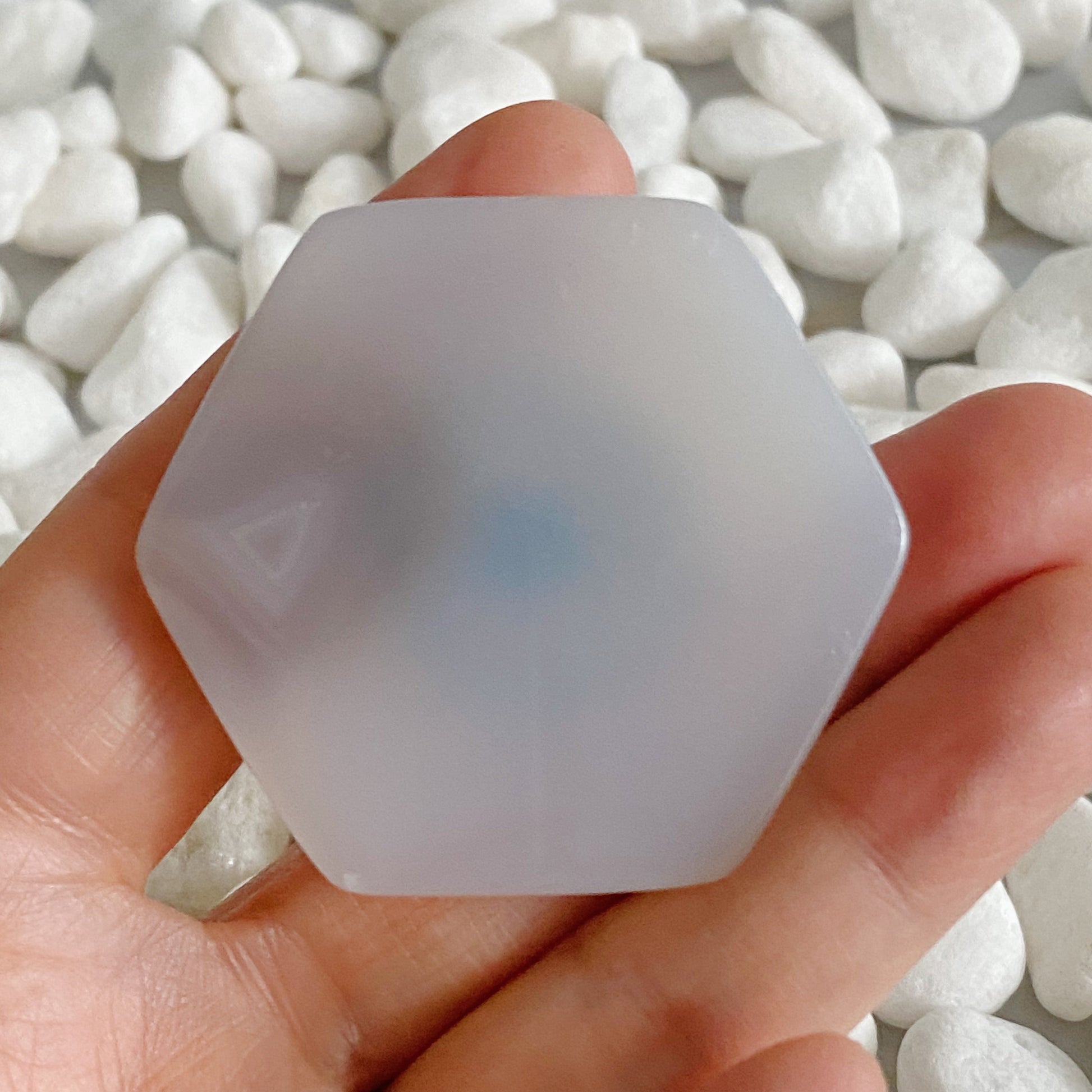 Clear silicone hexagonal object held in a hand with a blurred background of white stones.